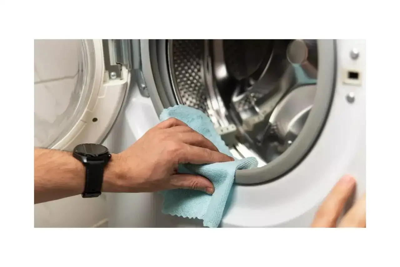 Mano limpiando la goma de la lavadora con un pa&ntilde;o azul para quitar mal olor ropa lavadora.