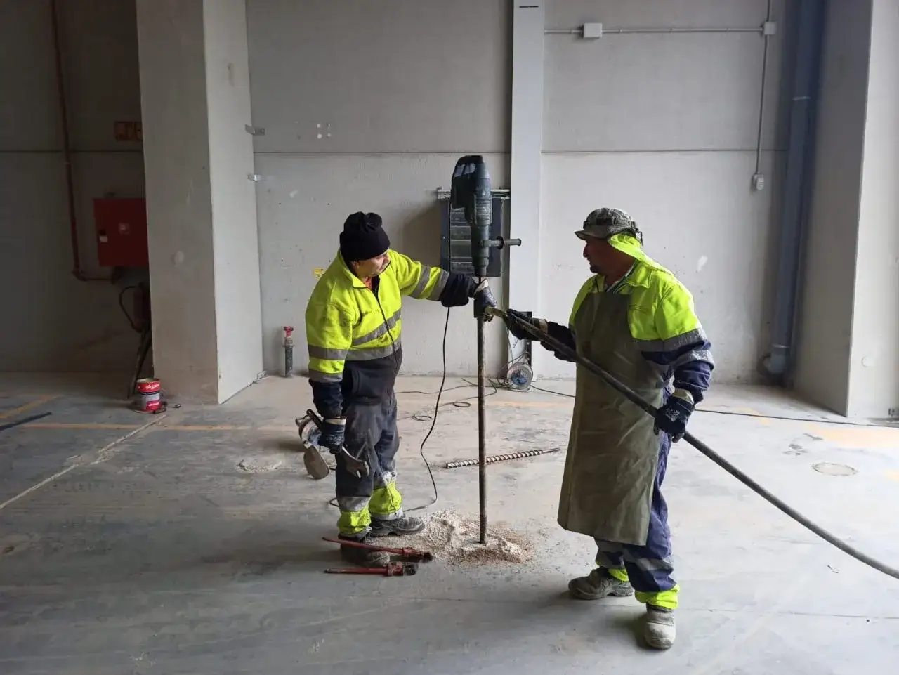 Dos obreros realizan trabajos de perforación para cemento inyectado en una obra.