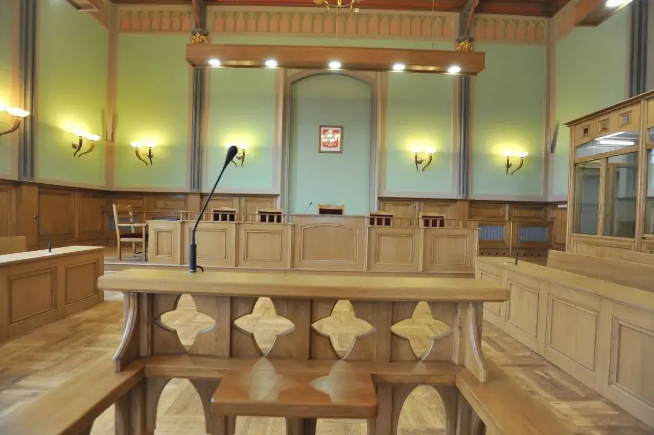 Pusta sala sądowa z drewnianymi ławami i mównicą. W tle godło Polski. To miejsce, gdzie zapadają decyzje, co oznacza oddalenie apelacji.