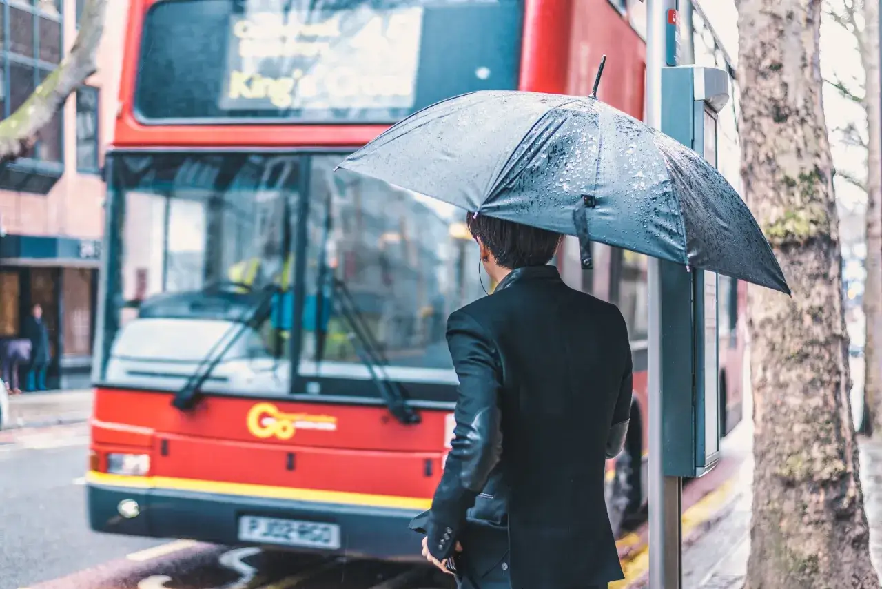 Deszczowy dzień w Londynie w listopadzie. Osoba z parasolką czeka na czerwony autobus.