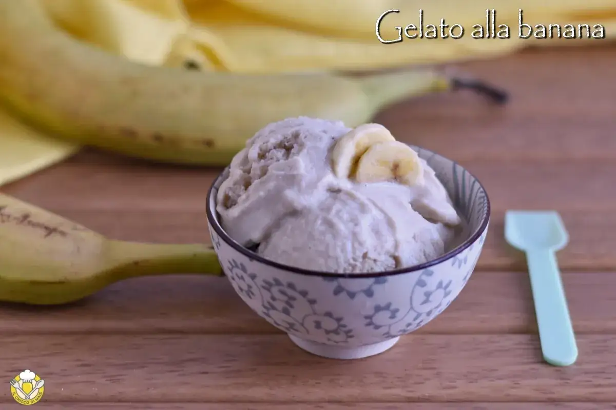 Una ciotola di cremoso gelato alla banana, guarnito con fettine di banana, su un tavolo di legno. Due banane intere sullo sfondo.