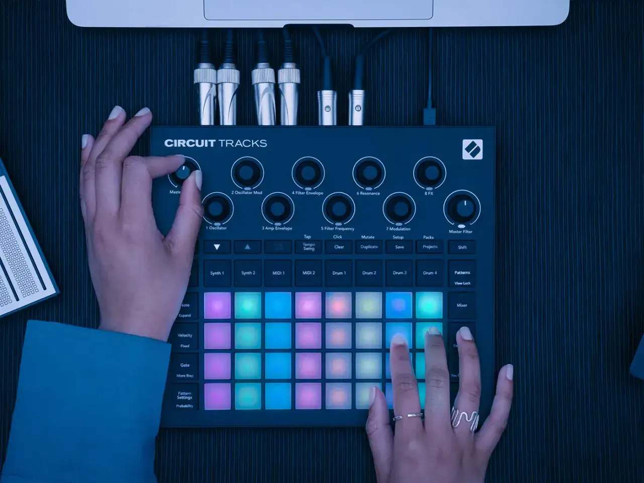 Ręce tworzą muzykę na Novation Circuit Tracks, naciskając kolorowe pady i kręcąc gałkami.