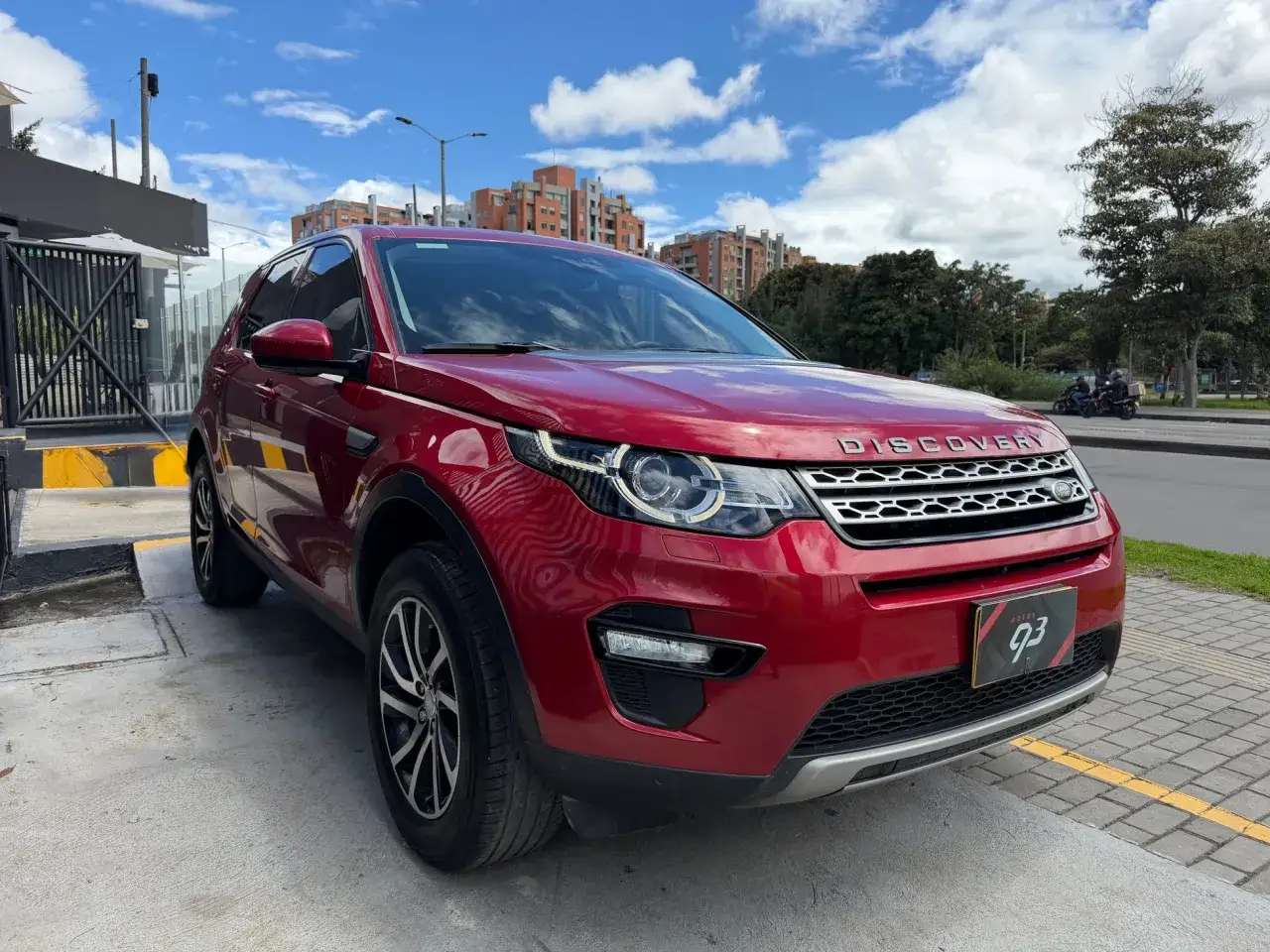 Un Land Rover Discovery HSE rojo brillante, listo para la aventura urbana bajo un cielo azul con nubes.
