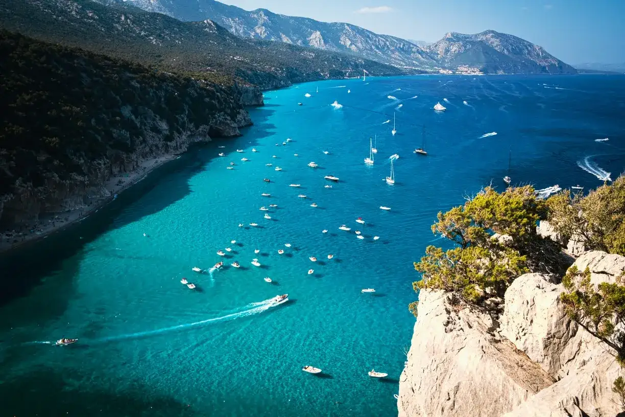 Una baia con acque turchesi e montagne sullo sfondo, piena di barche. Un vero gioiello tra le 20 spiagge più belle della Sardegna.