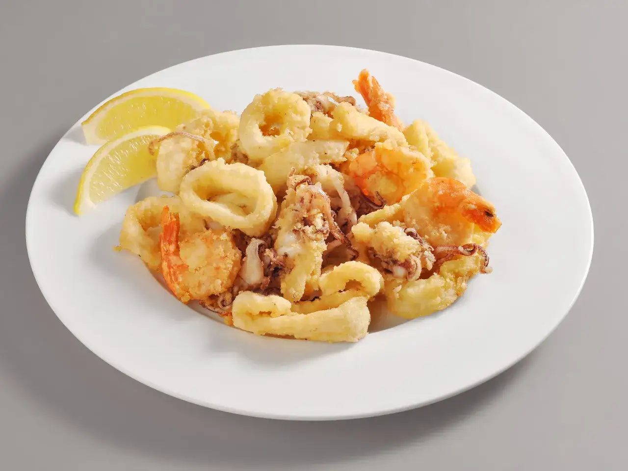 Un invitante piatto di frittura di pesce, con anelli di calamari dorati e gamberi croccanti, accompagnato da spicchi di limone fresco.