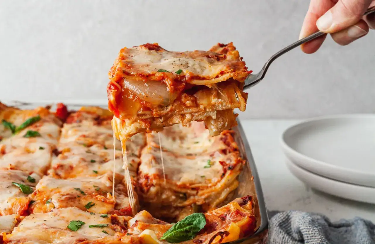 Une part généreuse de lasagnes aux légumes, recette italienne, est soulevée d'un plat. Le fromage fondant s'étire, révélant les couches de pâtes et de sauce tomate.