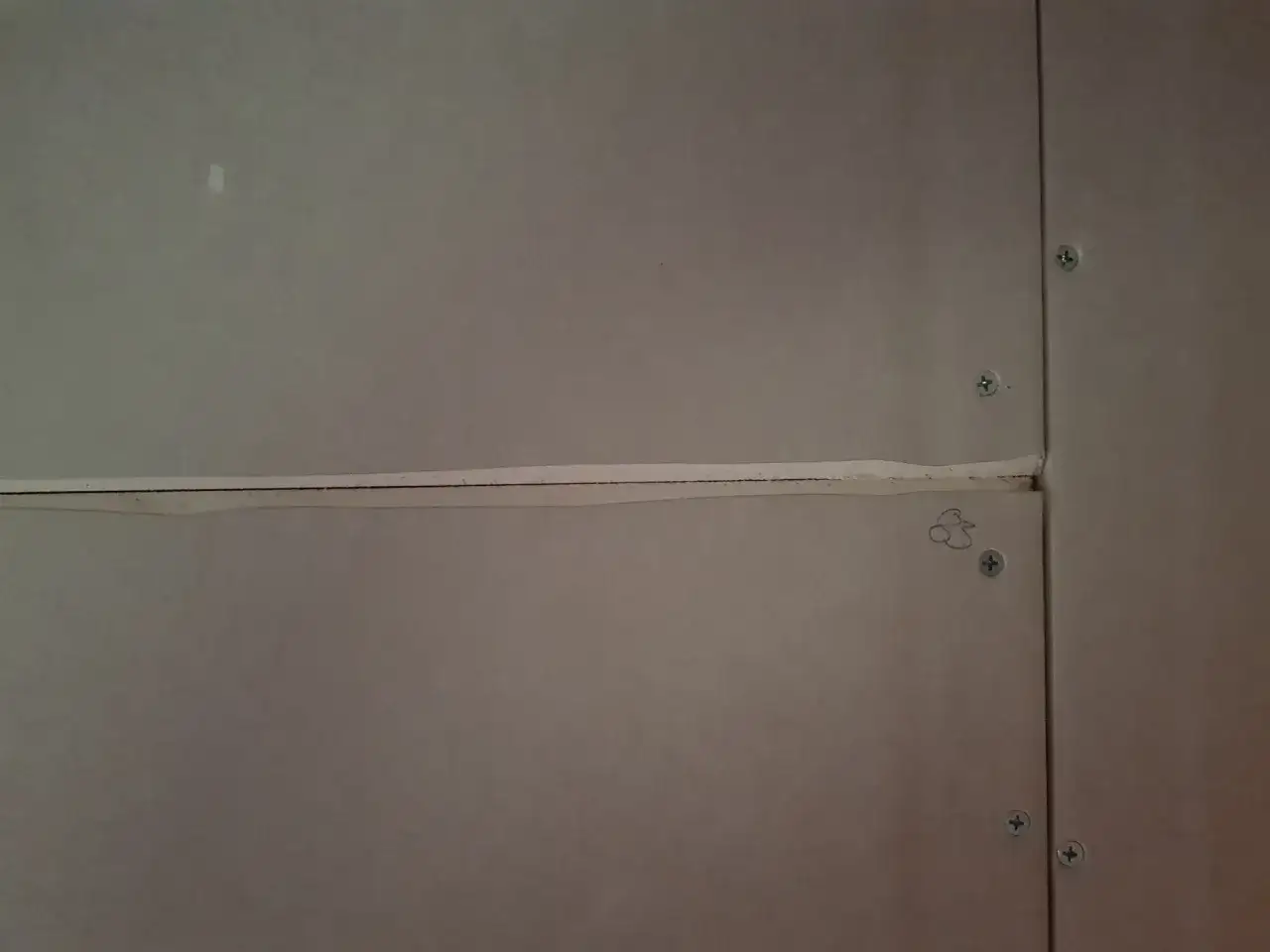 N&auml;rbild p&aring; gipsskivor d&auml;r skarvarna spacklas f&ouml;r att skapa en j&auml;mn yta. Skruvarna syns tydligt.