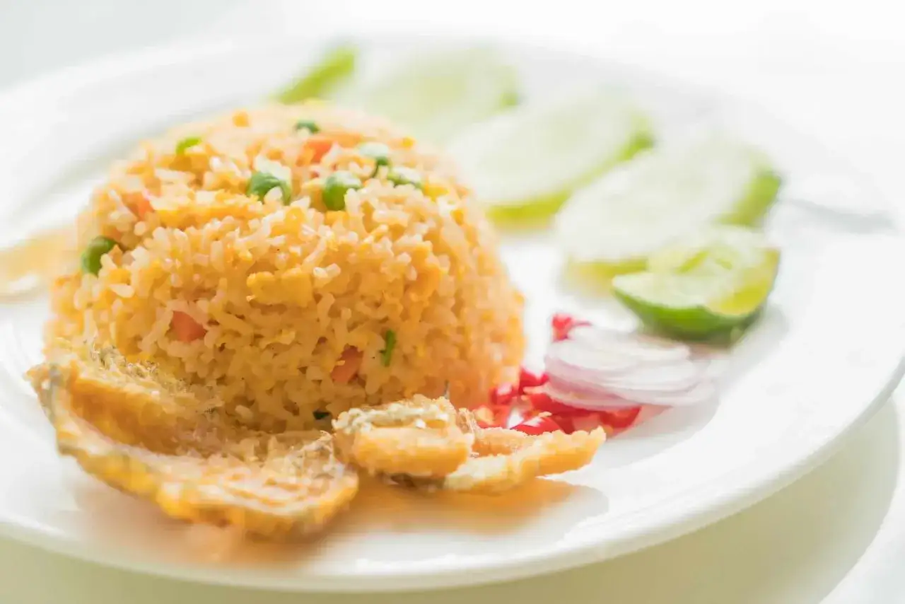 Delicioso arroz frito con guarnición de pepino, cebolla morada, chile y trozos de pescado frito.