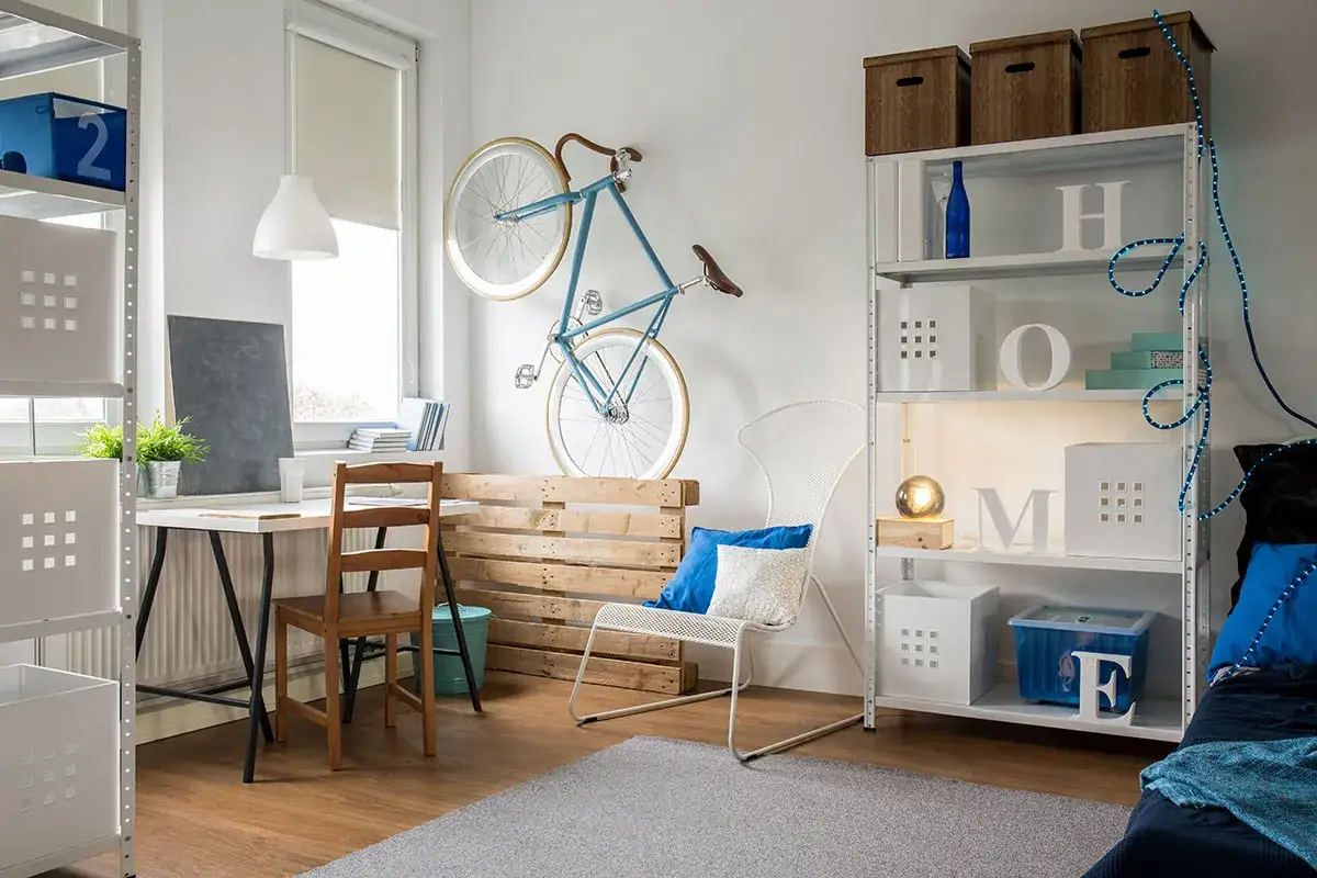 A small apartment furnished with a desk, chair, shelving unit, and a bicycle mounted on the wall. This space shows creative ways on how to furnish a small apartment.