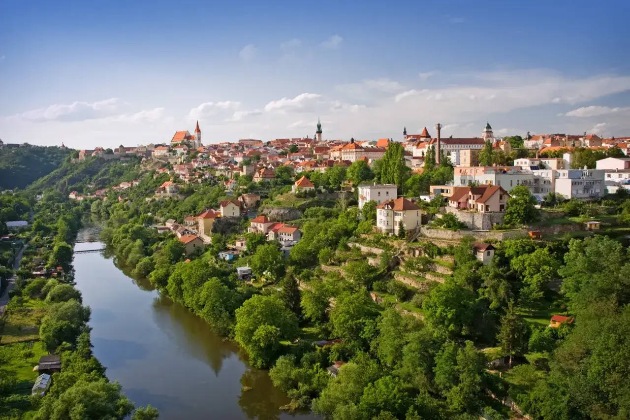 Znaim, Tschechien: malerische Stadt am Fluss mit roten D&auml;chern und gr&uuml;nen H&uuml;geln, die sich unter blauem Himmel erheben.