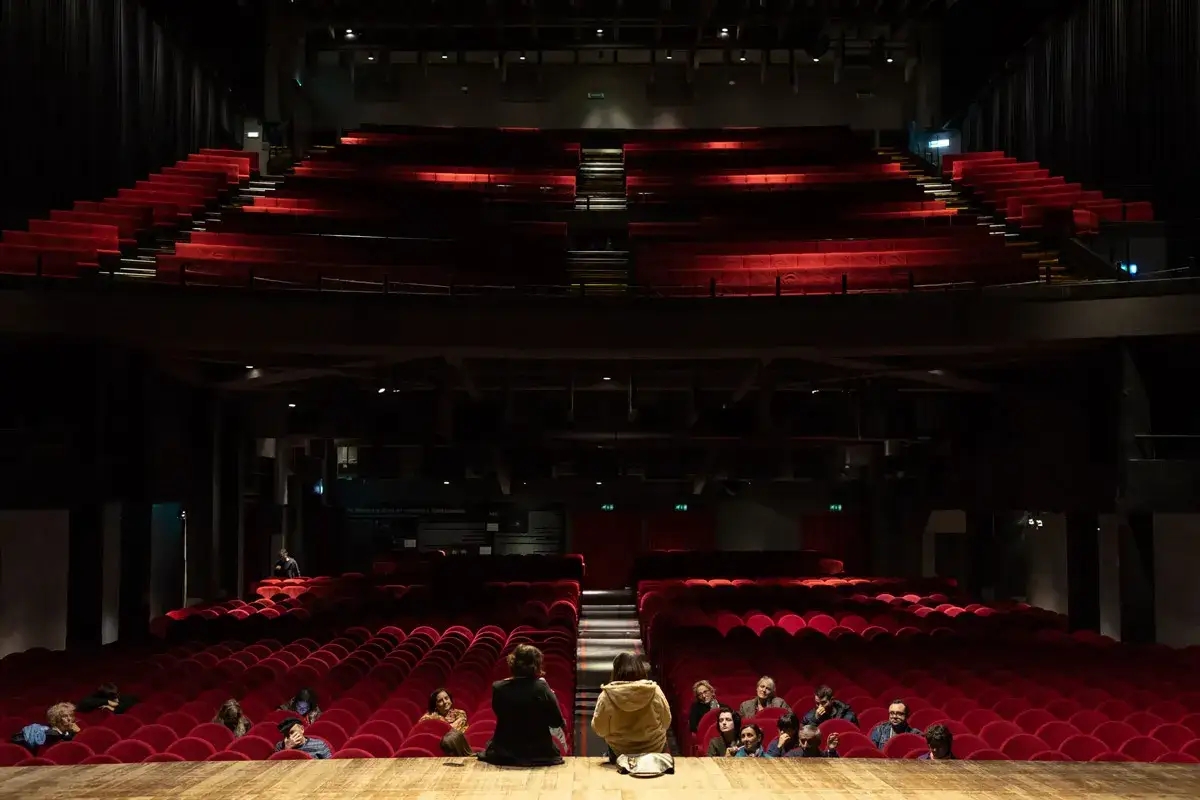 Il palco del Teatro Colosseo di Torino, con le poltrone rosse vuote e alcune persone sedute, in attesa del programma serale.
