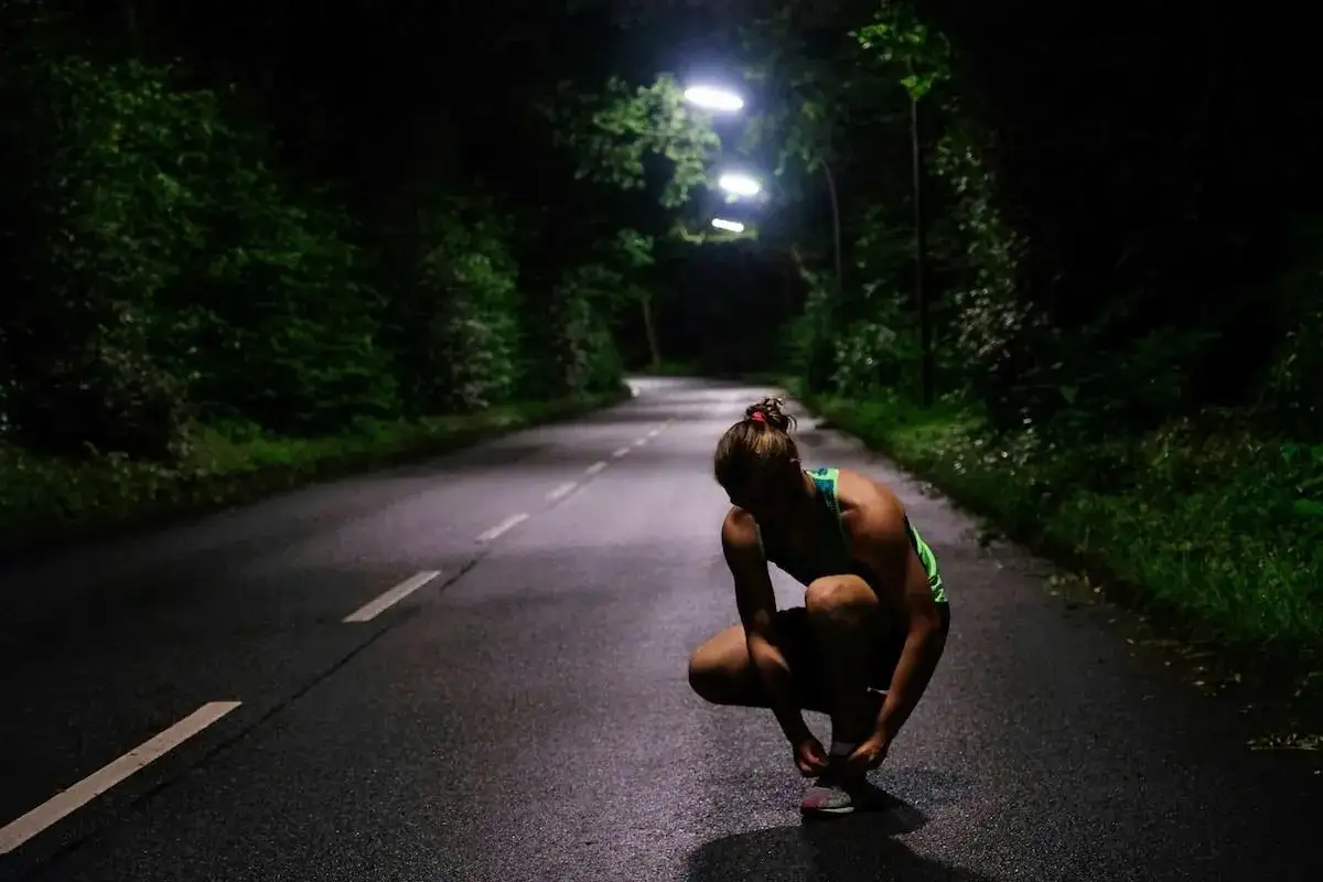 Atleta si allaccia le scarpe su una strada illuminata da lampioni, immersa nel buio. Le frasi sulla corsa risuonano nella sua mente.