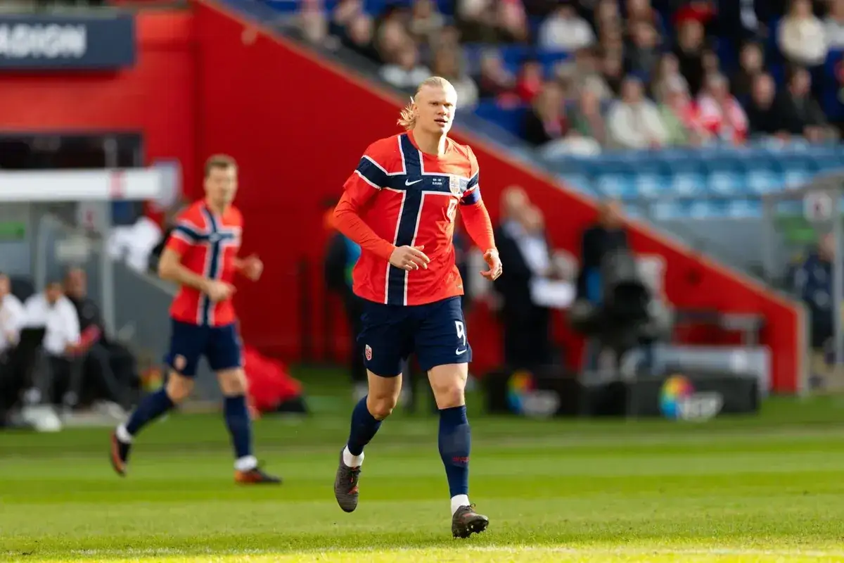 Erling Haaland w stroju Norwegii, biegnie po boisku. Jego zarobki budzą podziw, a forma na boisku zachwyca.