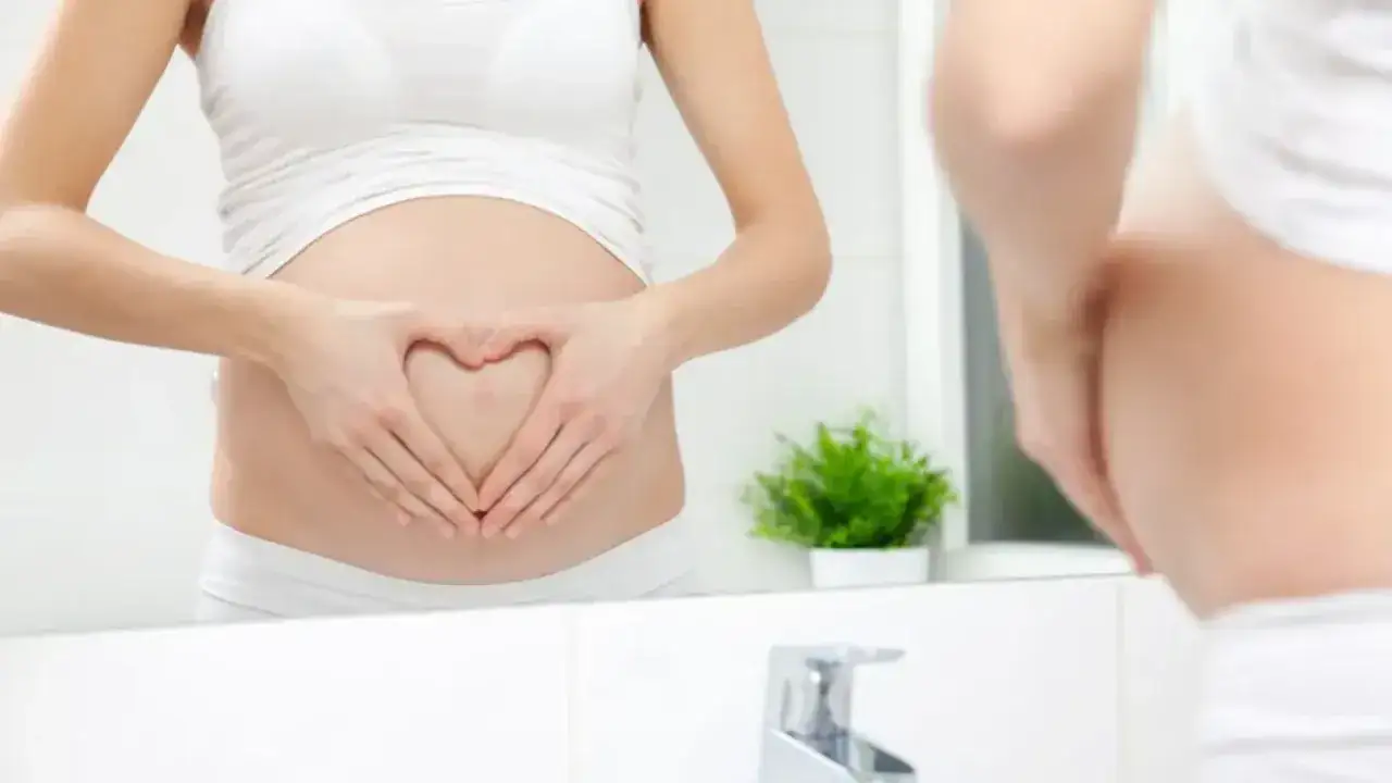 Brzuch ciężarnej kobiety z dłońmi ułożonymi w serce. Rozważasz czopki glicerynowe w ciąży?