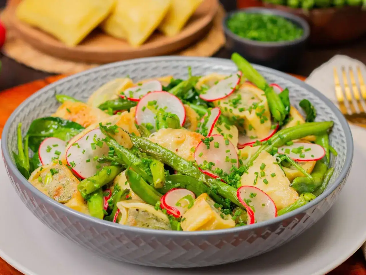 Ein k&ouml;stlicher Maultaschen Salat mit knackigen gr&uuml;nen Bohnen, Radieschen und frischem Schnittlauch in einer grauen Sch&uuml;ssel.