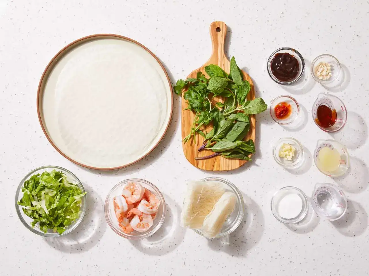 Składniki do przygotowania świeżych spring rolls: papier ryżowy, krewetki, warzywa, zioła, makaron ryżowy i sosy.
