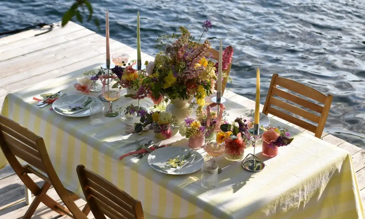Vacker dukning vid vattnet med blommor och ljus. Perfekt middagstips helg för en sommarkväll.