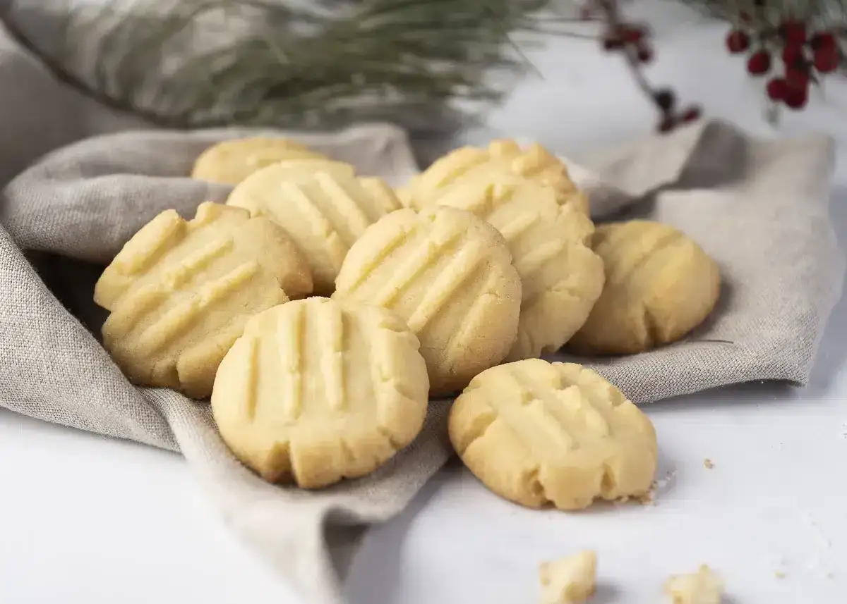 Montón de galletas de mantequilla doradas, con un patrón de líneas en relieve, servidas sobre una tela gris.