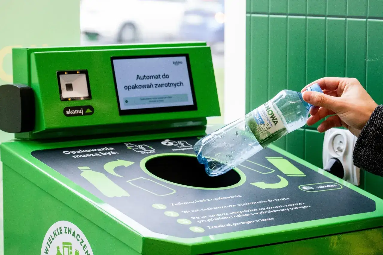 Ręka wrzuca plastikową butelkę do automatu, kt&oacute;ry jest częścią systemu kaucyjnego w Niemczech.