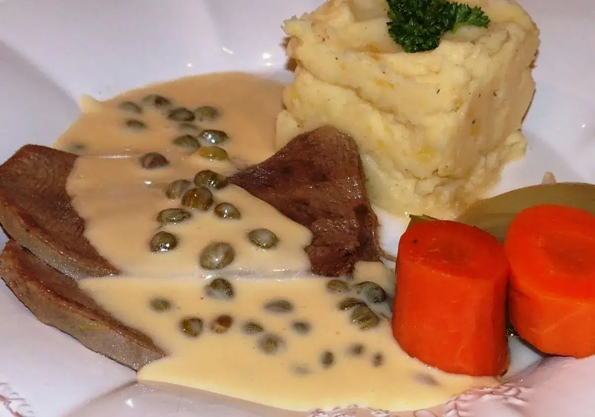 Tranches de langue de bœuf nappées d'une sauce crémeuse aux câpres, accompagnées de purée de pommes de terre et de carottes.