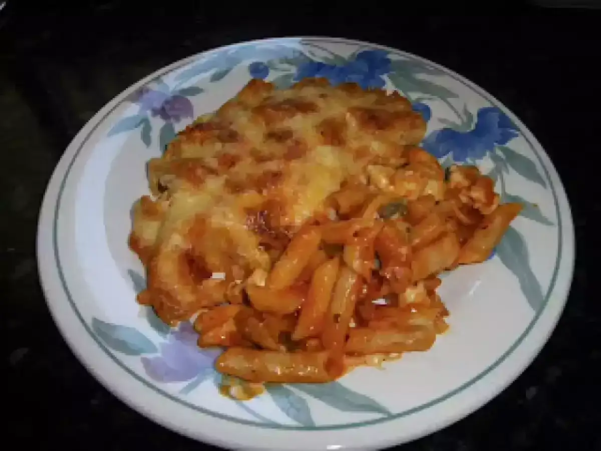 Plato de macarrones con pollo gratinados, cubiertos de queso derretido y salsa roja.