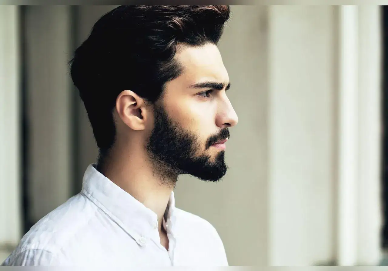 Profil d'un homme à la barbe soignée et aux cheveux courts, portant une chemise blanche.