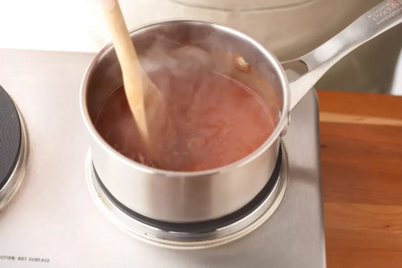 Cuchara de madera removiendo salsa roja humeante en una olla, un paso clave para saber como espesar una salsa.
