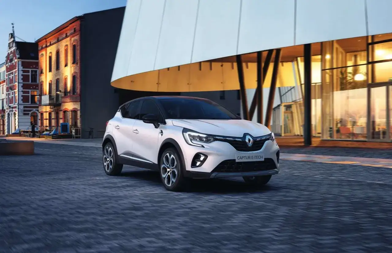 Renault Captur E-Tech, un'auto moderna che si muove con agilità in un paesaggio urbano serale, tra architetture suggestive e luci soffuse.