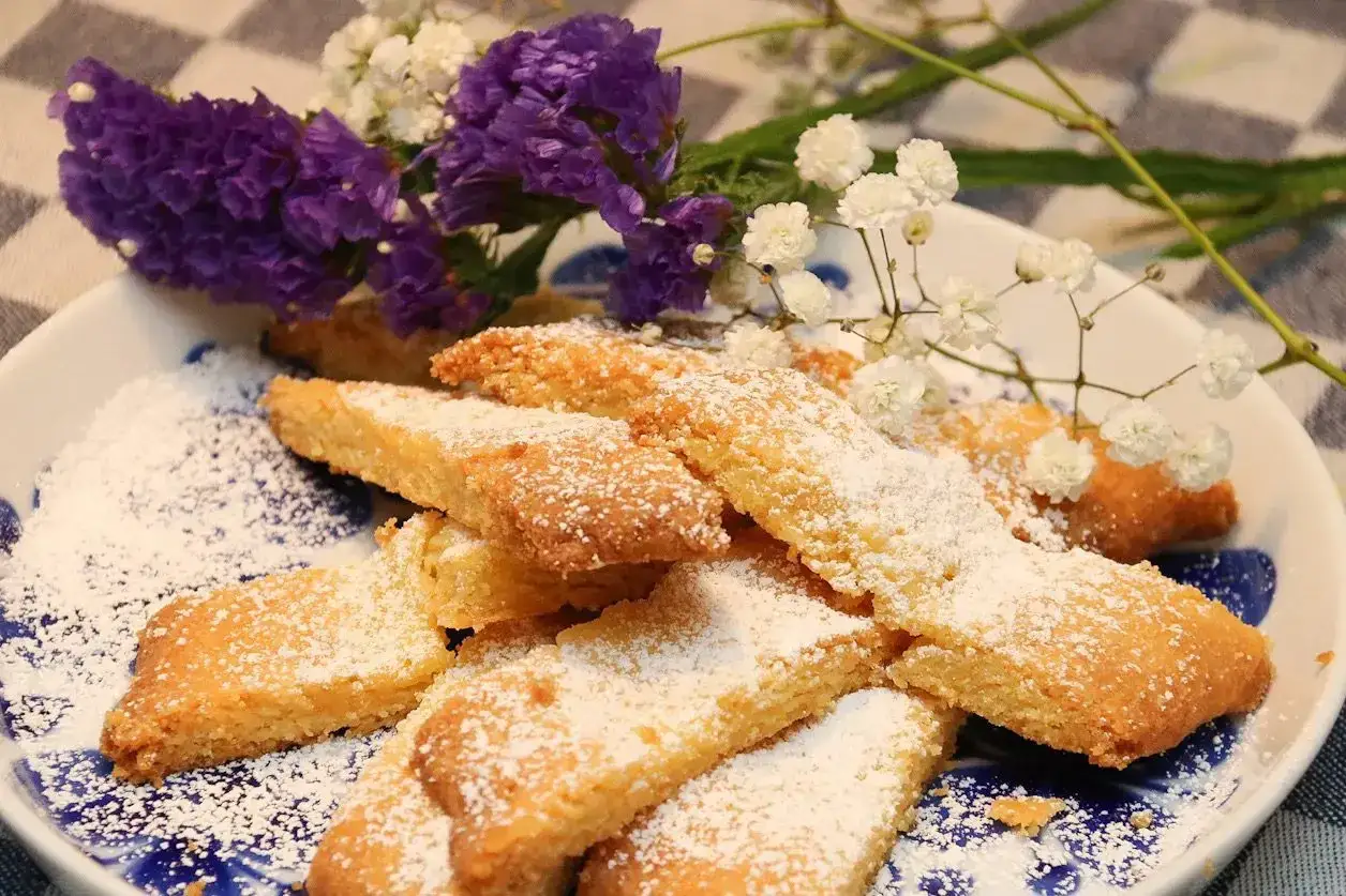 En tallrik med gyllene, mjuk kaka, pudrad med florsocker, prydd med lila och vita blommor.