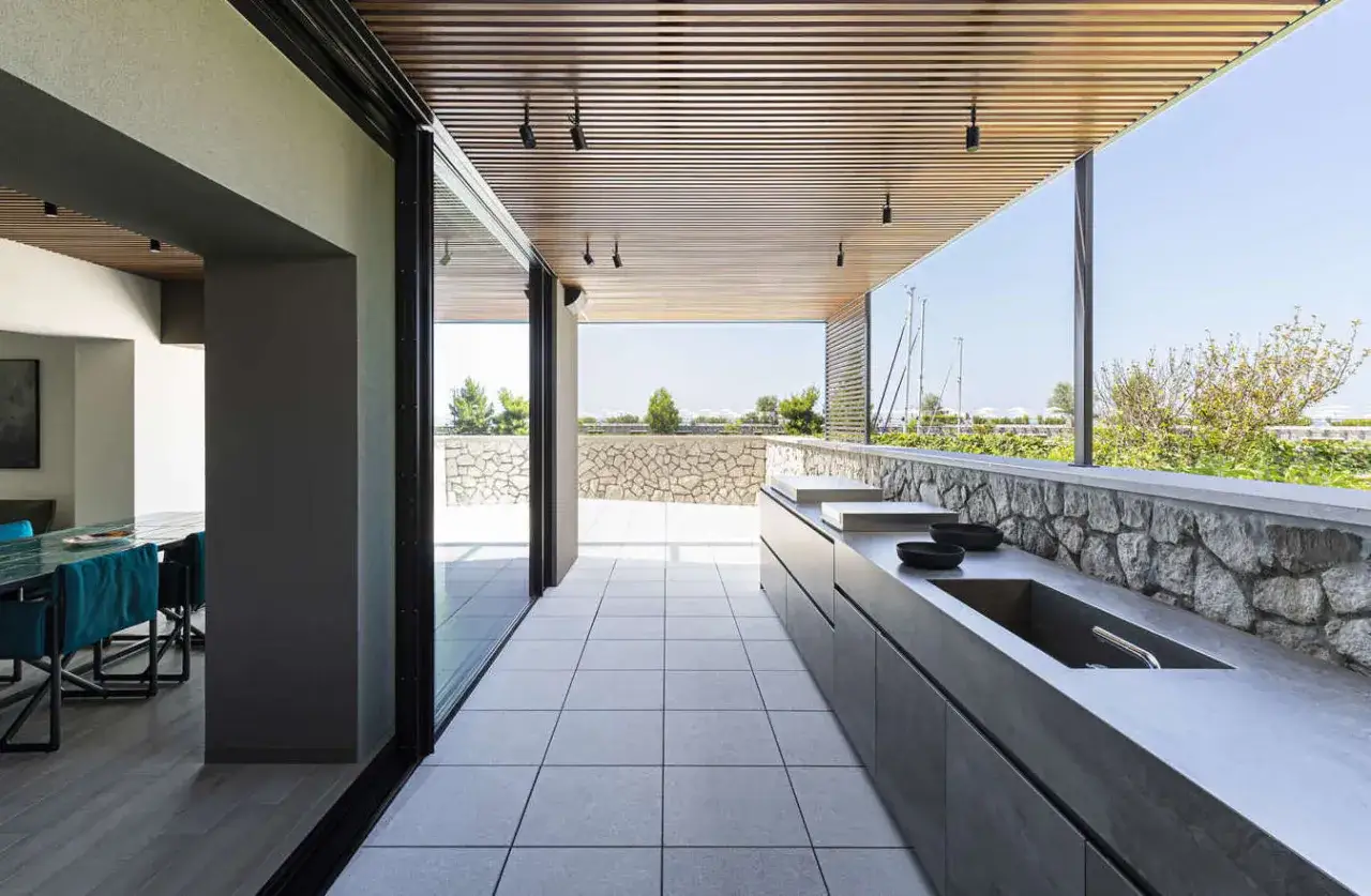 Moderna veranda con cucina esterna, piano in cemento e vista sul verde. Ideale per cene all'aperto.