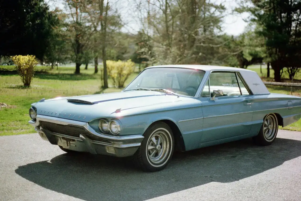 Błękitny Ford Thunderbird z 1963 roku, klasyk motoryzacji, zaparkowany na tle drzew.