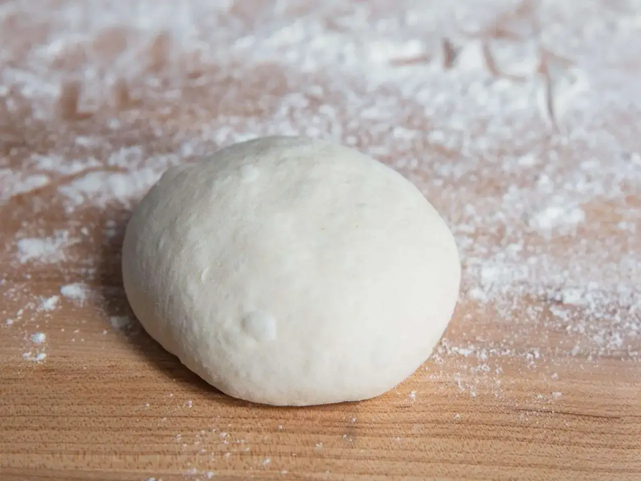 En rund boll av pizzadeg 6 timmar, redo att bakas, ligger p&aring; ett mj&ouml;lat tr&auml;bord.