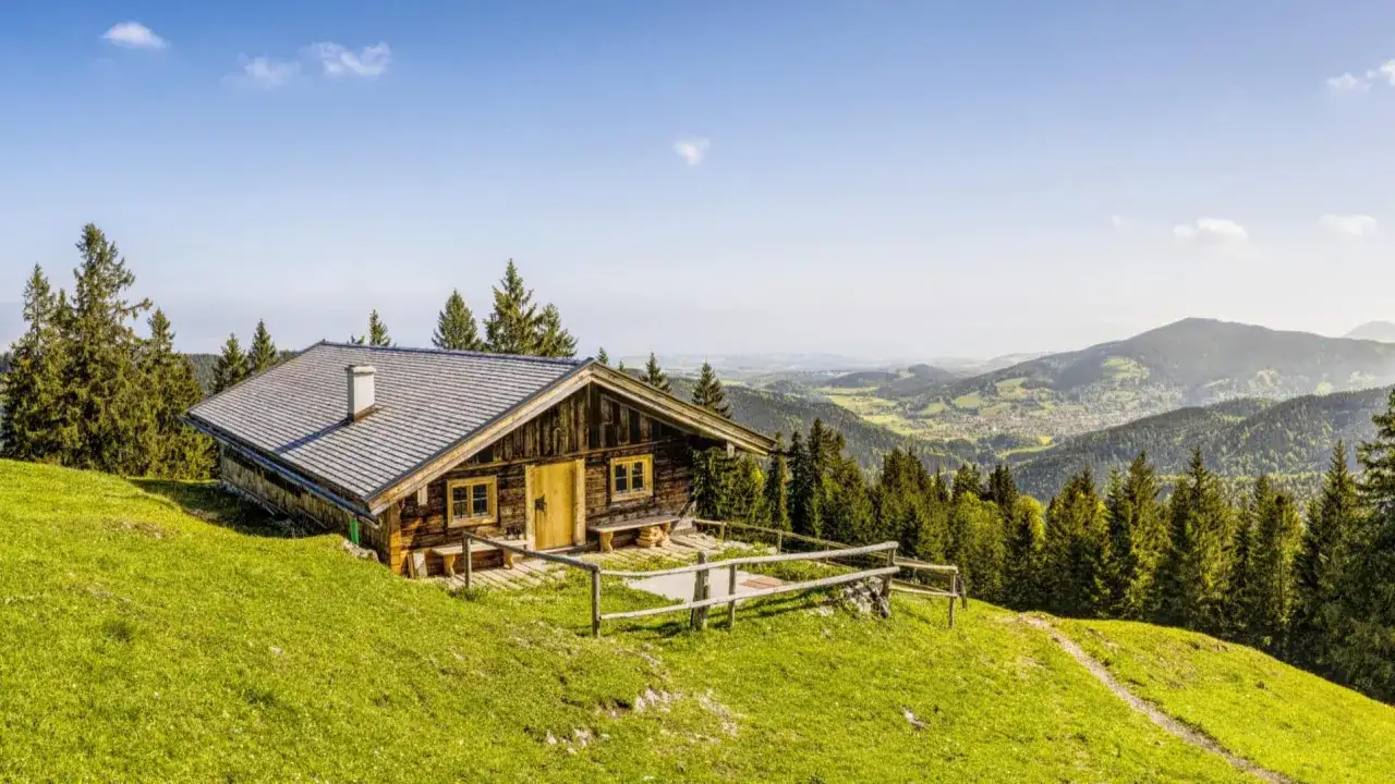 Holzhütte auf einer grünen Alm mit Blick ins Tal. Hier kann man erleben, was ist eine Alm: ein Ort der Ruhe und Natur.