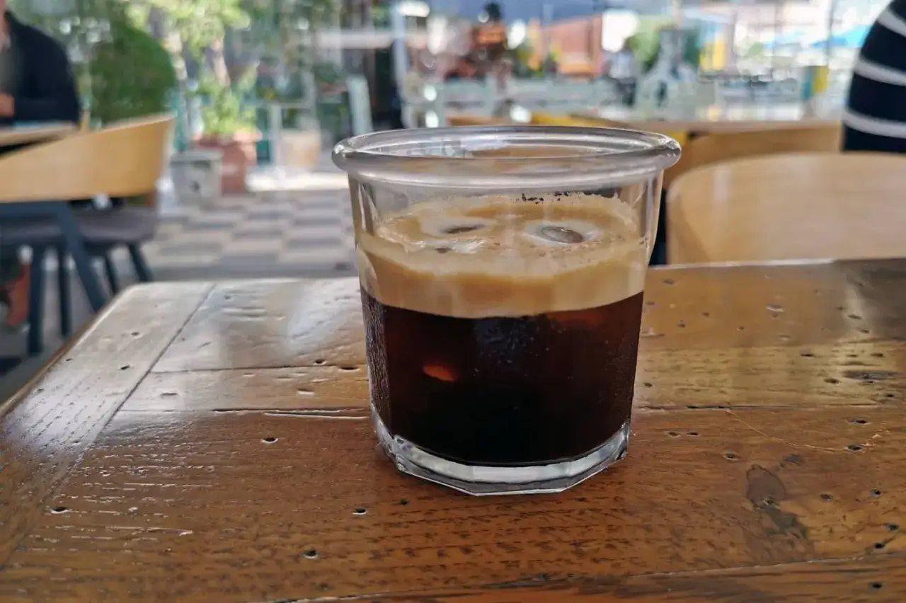 Orzeźwiający freddo espresso z grubą pianką na wierzchu, podany w szklance na drewnianym stole. Idealny na gorący dzień.