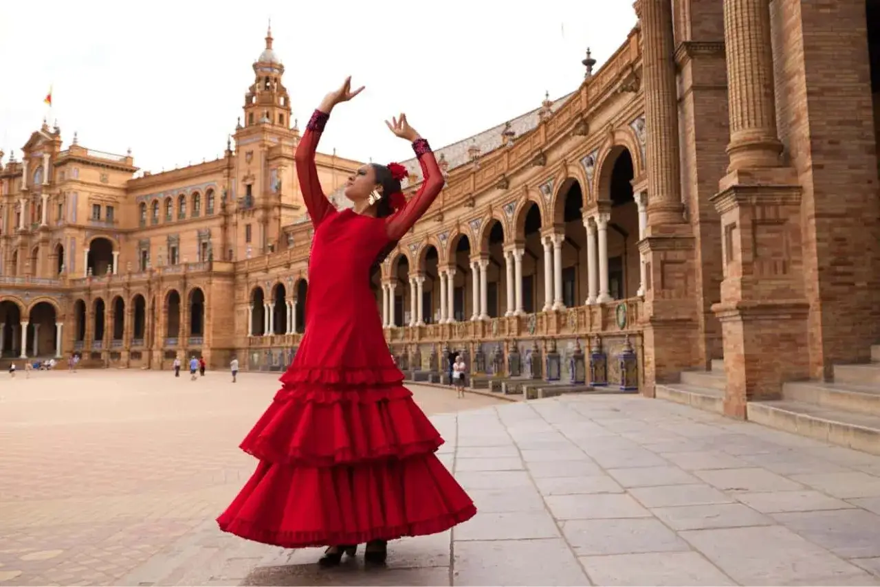 Bailarina con vestido rojo, brazos en alto, lista para aprender flamenco en la Plaza de Espa&ntilde;a.