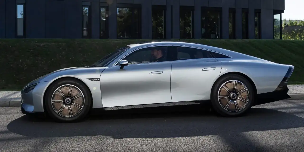 Silberner Mercedes EQXX gleitet elegant an einem modernen Geb&auml;ude vorbei.