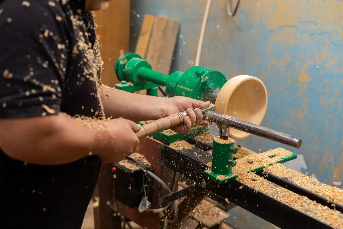 Artisan façonnant un bol en bois sur un tour. Démonstration de ce que faire avec un tour à bois, créant des copeaux volants.