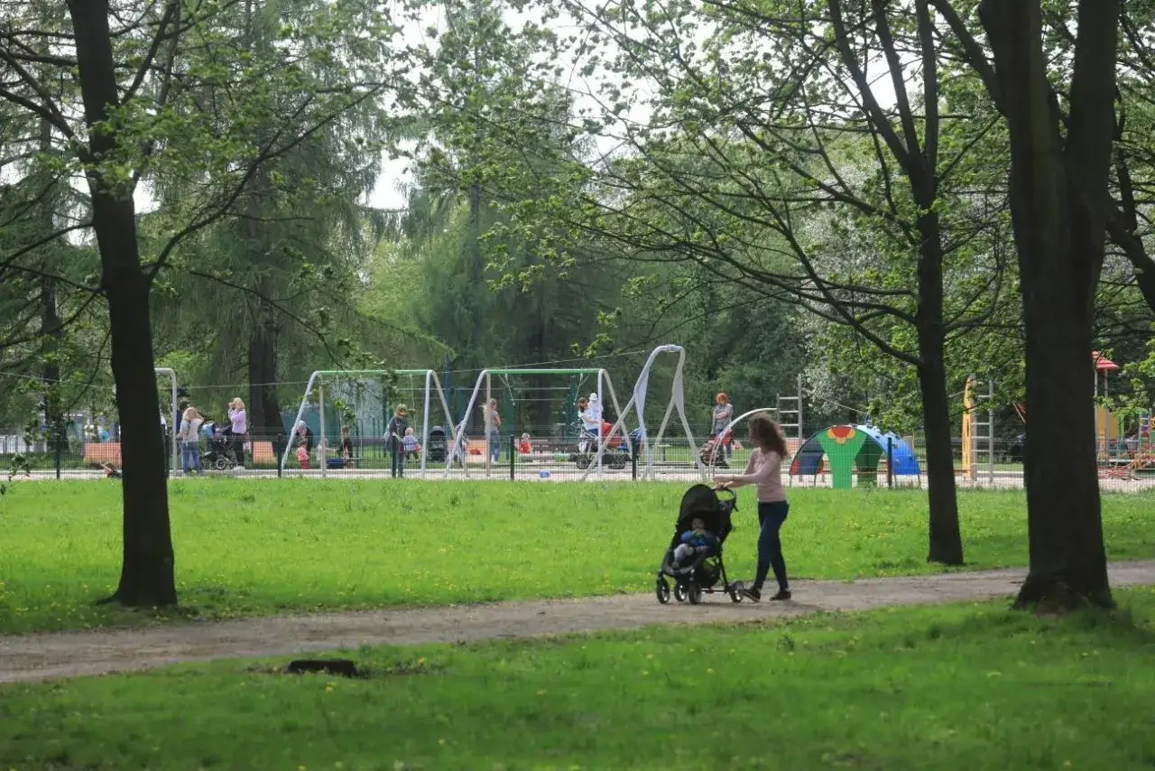 Kobieta spaceruje z wózkiem po parku, zastanawiając się, po jakim czasie przedstawić dziecku nowego partnera. W tle plac zabaw.