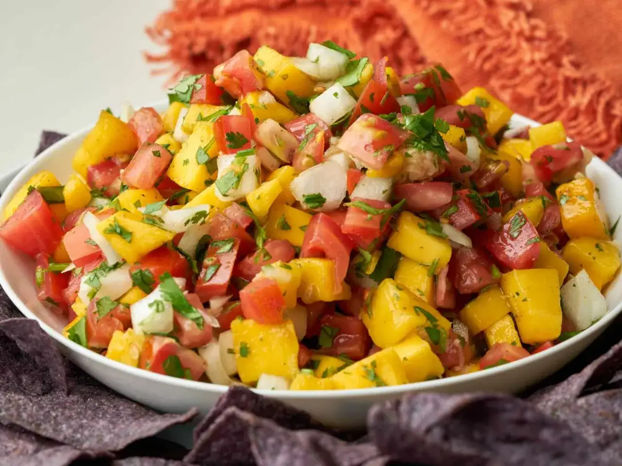 Bunte Mango Salsa mit Tomaten, Zwiebeln und Koriander in einer Schüssel, serviert mit Tortilla-Chips.