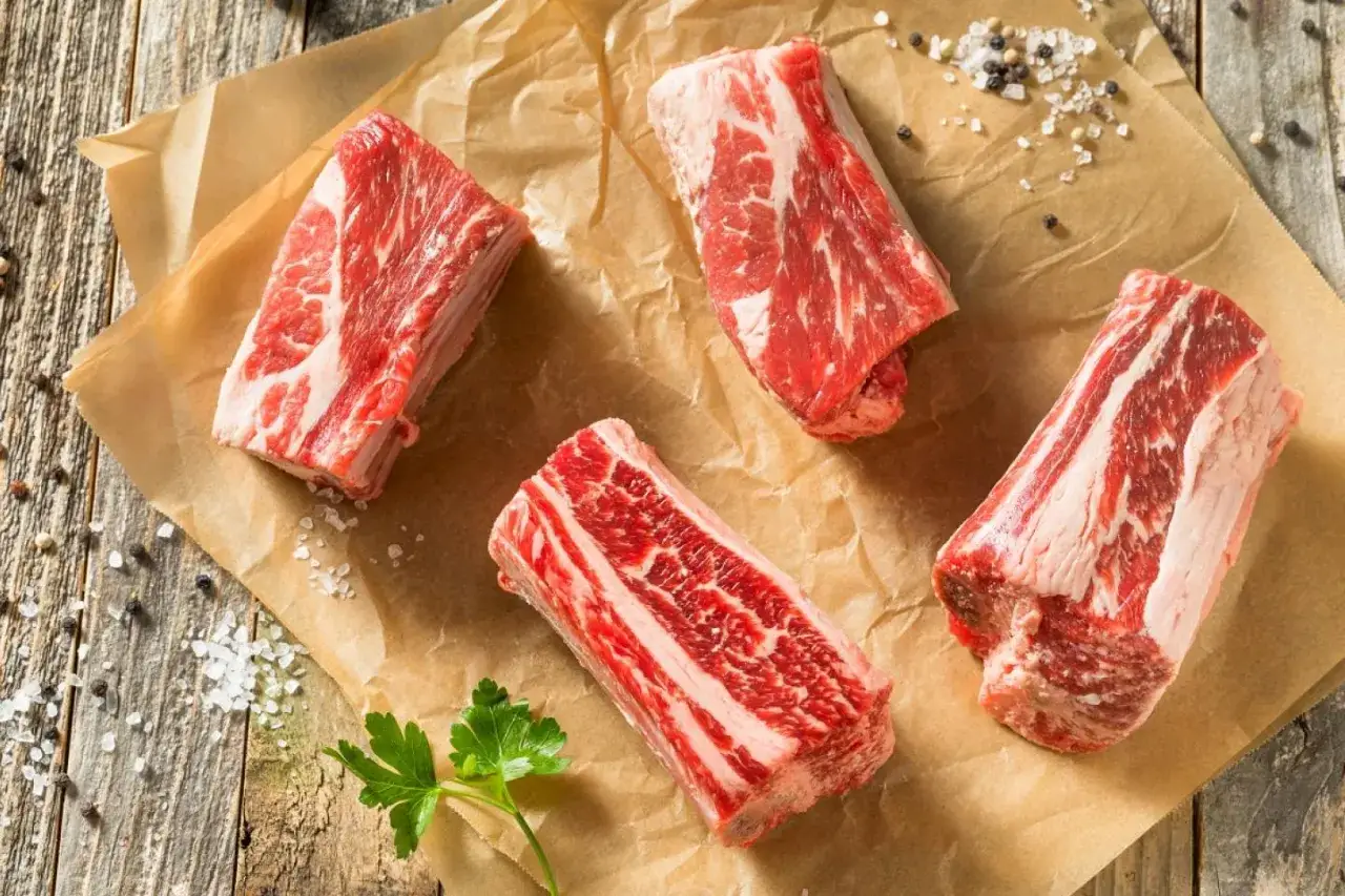 Quatre morceaux de plat de côte cru, prêts pour le temps de cuisson au four. Sel et poivre parsèment le papier cuisson.