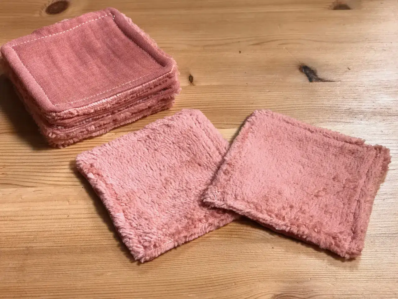 Pile de carrés roses en tissu doux, parfaits comme gabarit lingettes lavables. Deux lingettes sont posées à côté.