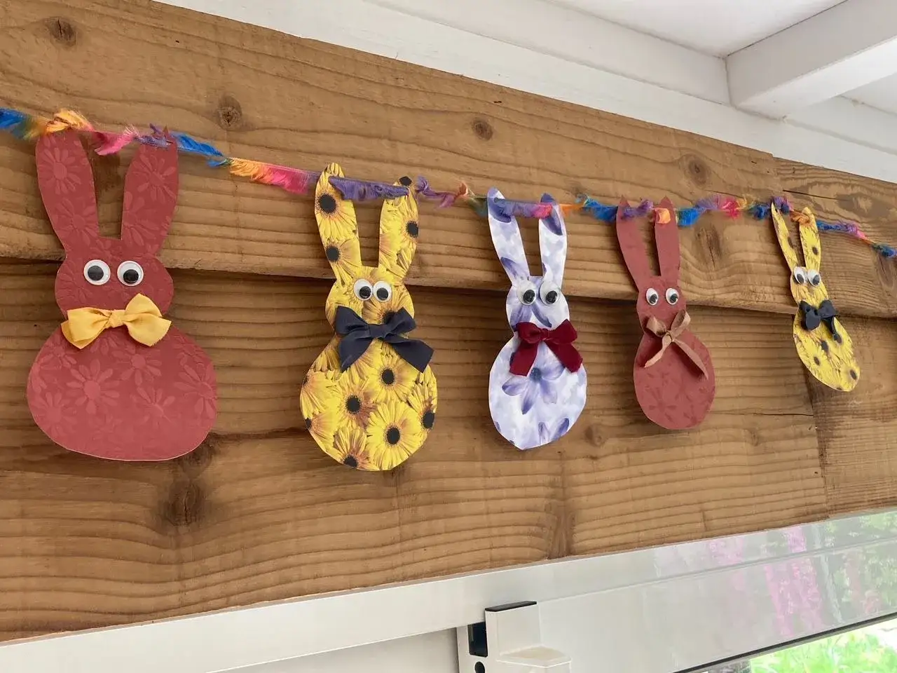 Guirlande de lapins colorés, déco de Pâques à faire soi-même avec récup. Des lapins en papier aux motifs variés, ornés de nœuds et d'yeux rigolos, suspendus à une ficelle multicolore.