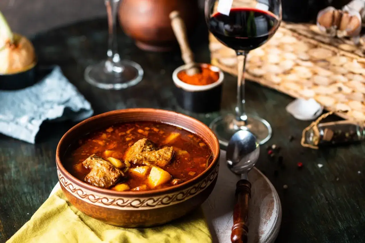 Un saporito goulash, perfetto per scoprire cosa mangiare a Trieste, accompagnato da un bicchiere di vino rosso.