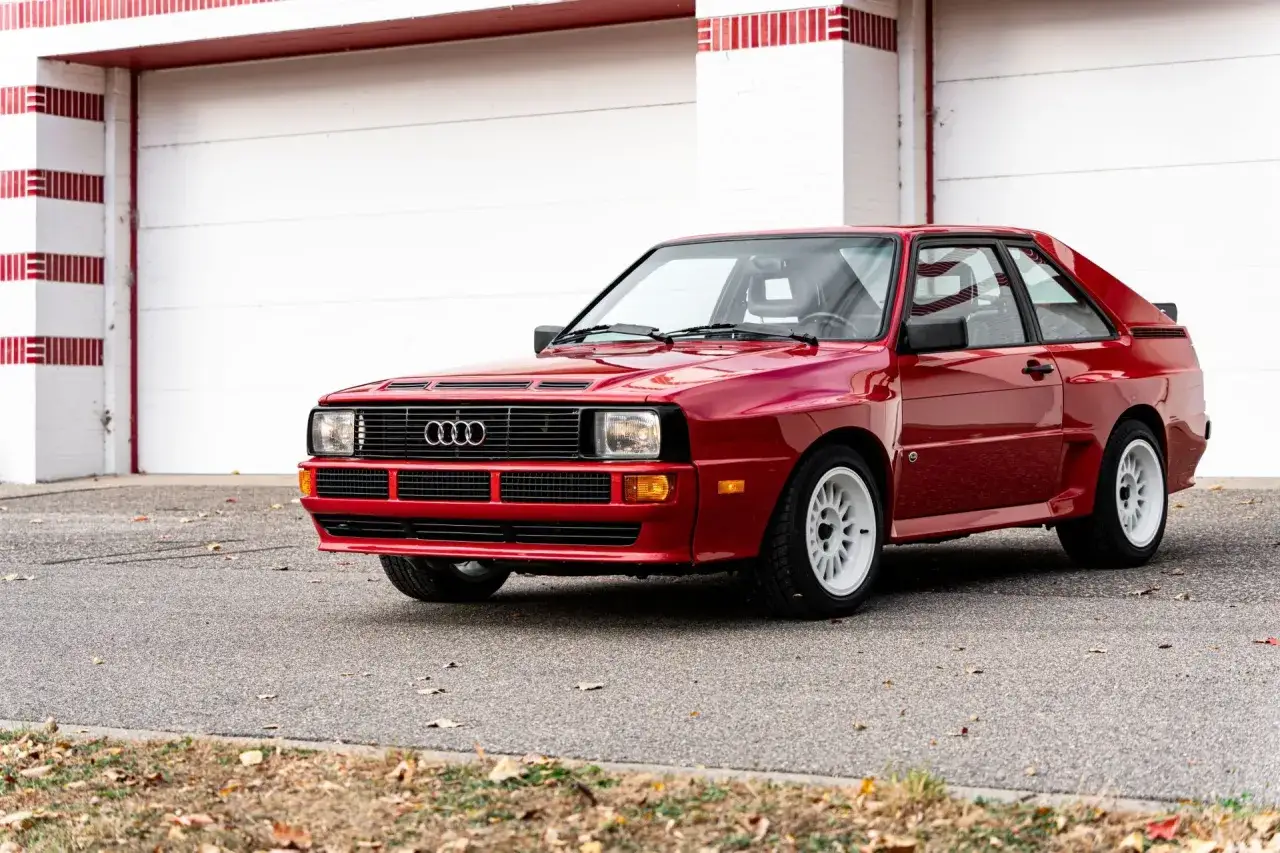 Czerwony Audi S1 Quattro z białymi felgami stoi przed garażem.