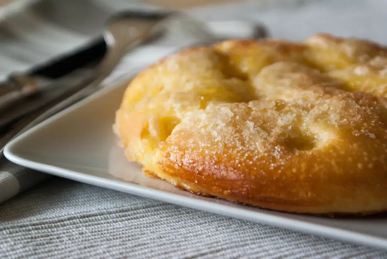 Une tarte au sucre dorée, saupoudrée de cristaux brillants, repose sur une assiette blanche. Un délice simple et gourmand.