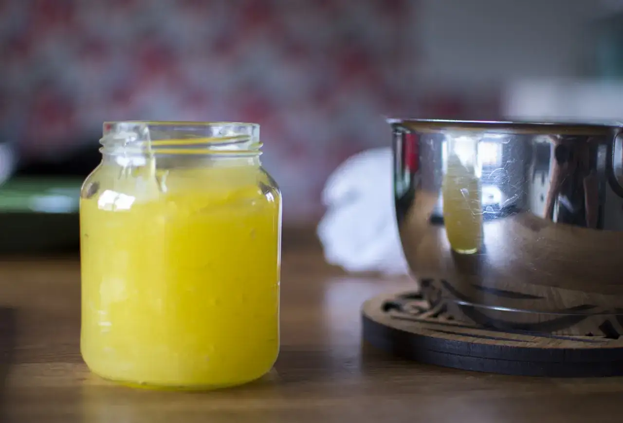 En burk med hemgjord lemon curd, perfekt för ditt nästa recept. Bredvid står en skål i metall.
