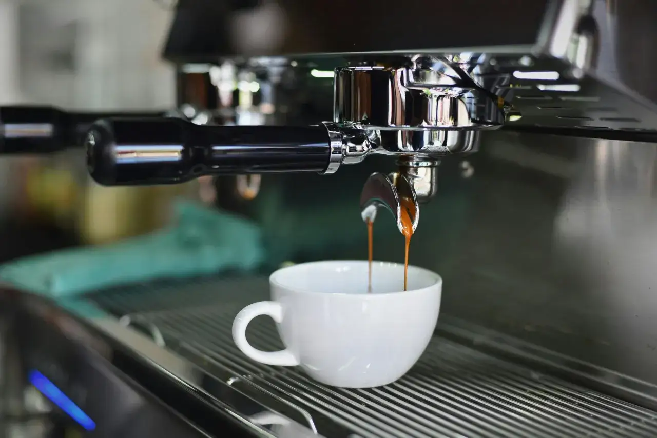 Espresso che cola in una tazzina bianca, parte del processo di consumo macchina caffè.