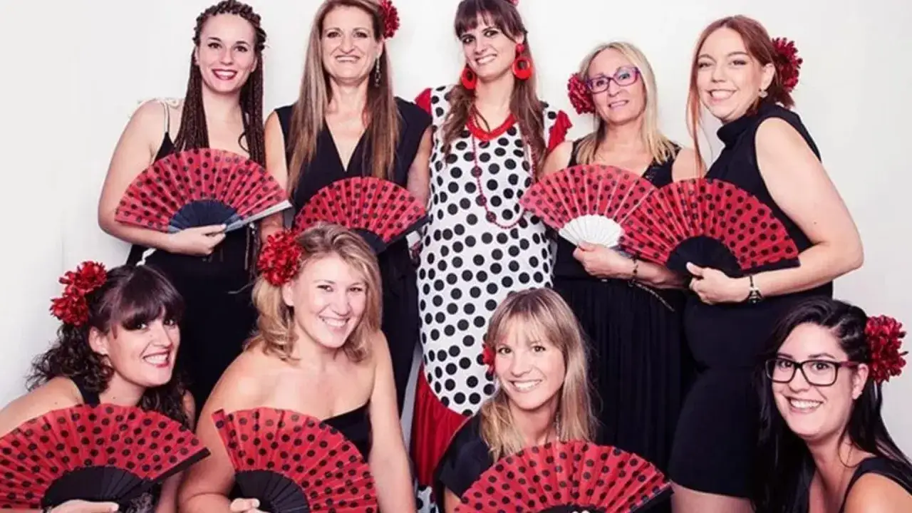 Grupo de mujeres sonriendo y sosteniendo abanicos rojos con lunares negros, listas para organizar despedida de soltero.