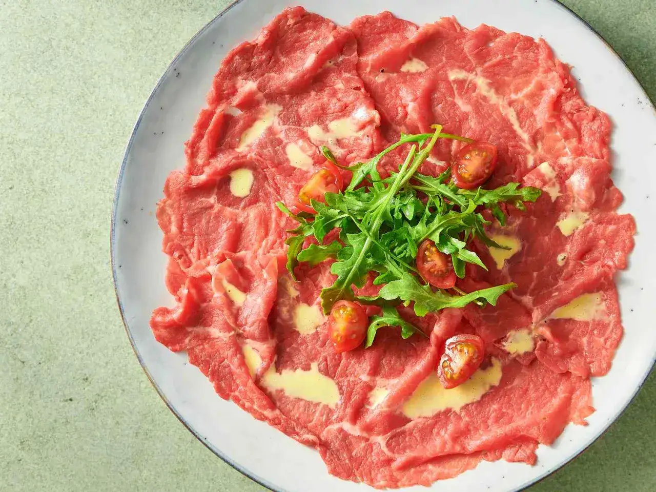 Tunnskivad carpaccio di manzo med ruccola och körsbärstomater. En delikat förrätt som väcker aptiten.