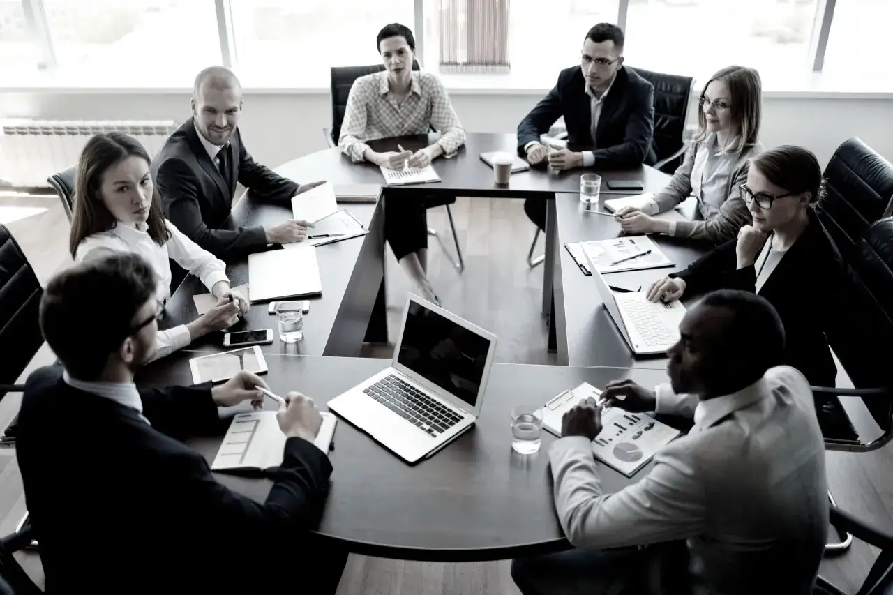A diverse team collaborates around a conference table, reviewing documents and laptops as part of a chro program.